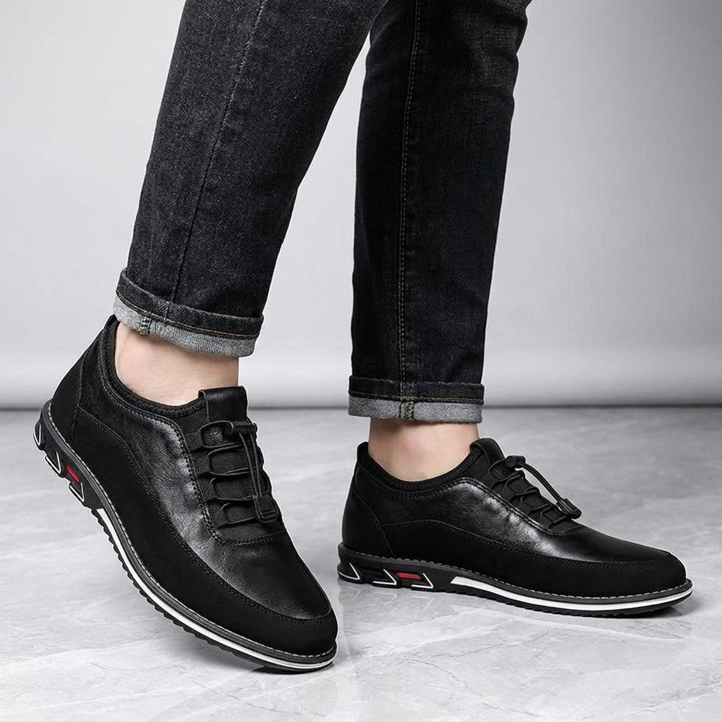 Sutri Leather Slip-On Shoes — Black, worn with dark cuffed jeans, knee-down view on light-grey marble