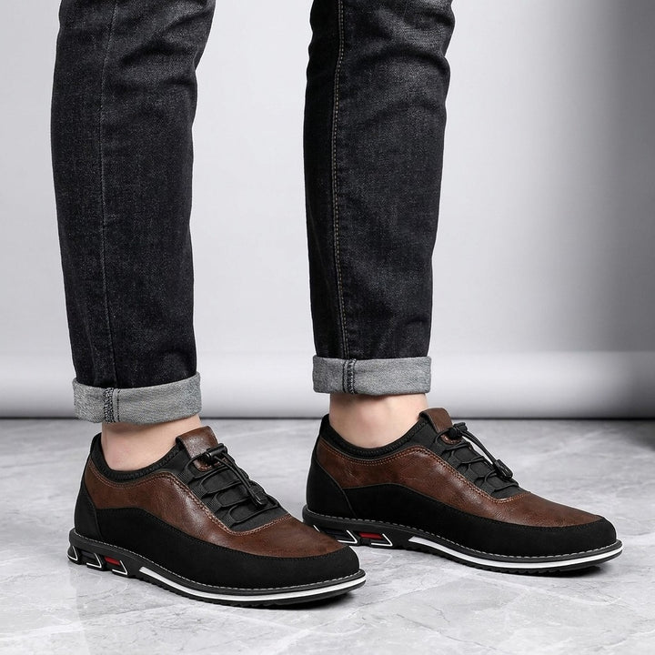 Sutri Leather Slip-On Shoes — Chestnut Brown, worn with dark cuffed jeans, knee-down view on light-grey marble