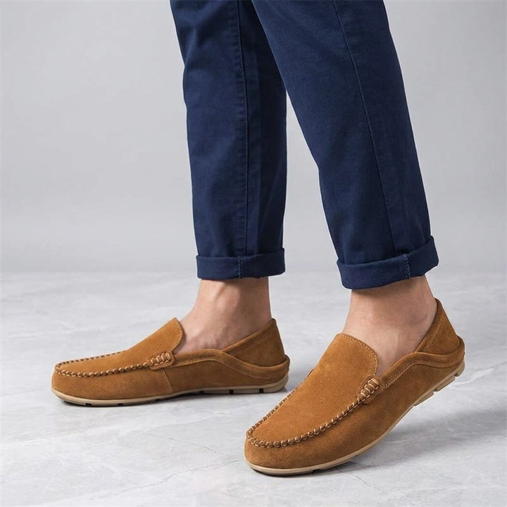 Menaggio Suede Loafers — Apricot, worn sockless with cuffed navy chinos, knee-down on light grey marble
