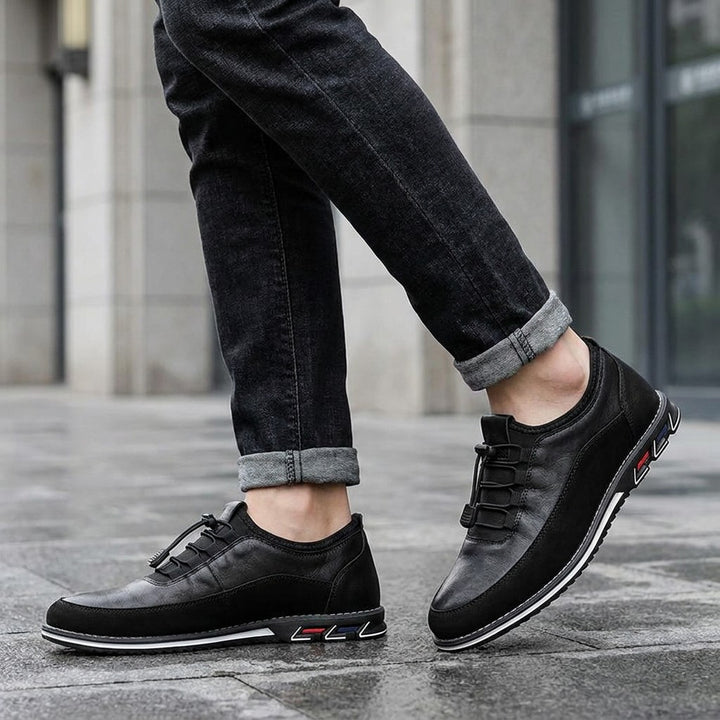 Sutri Leather Slip-On Shoes — Black, worn with dark cuffed jeans on a city sidewalk outside an office building
