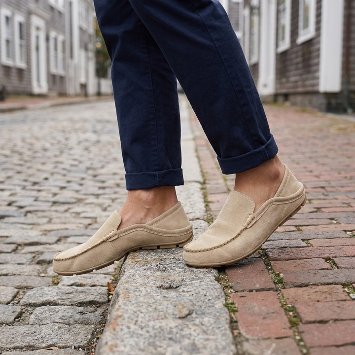 Menaggio Suede Loafers — Khaki, worn sockless with cuffed navy chinos on a cobblestone street curb