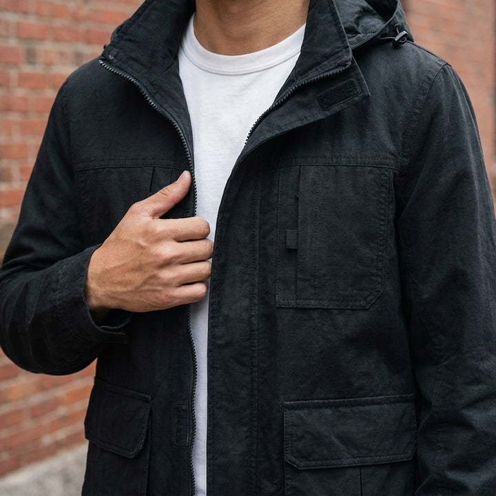 Close-up of the Pavia Hooded Cargo Jacket in Black worn over a white tee, showing the stand collar, hood and velcro chest pockets