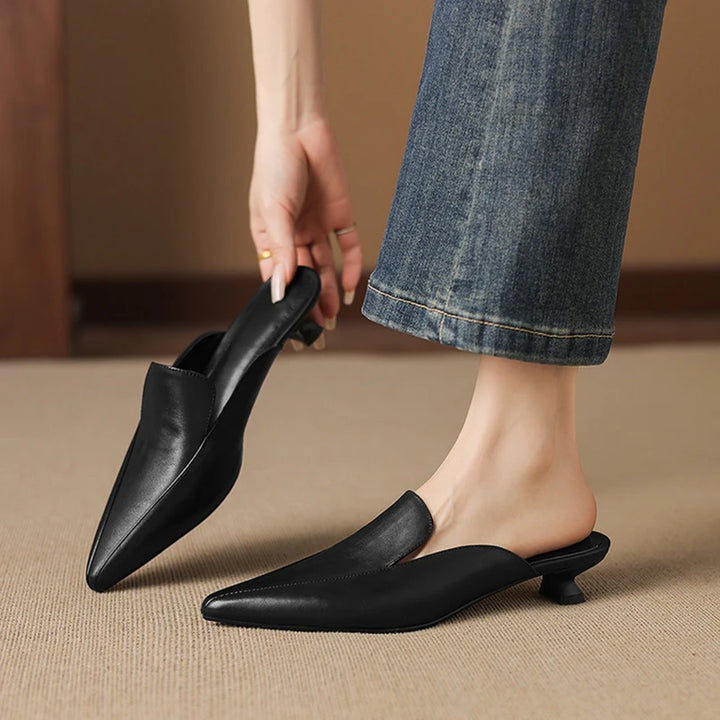 Cervia Leather Mules — Black, worn with blue jeans, one shoe held in hand
