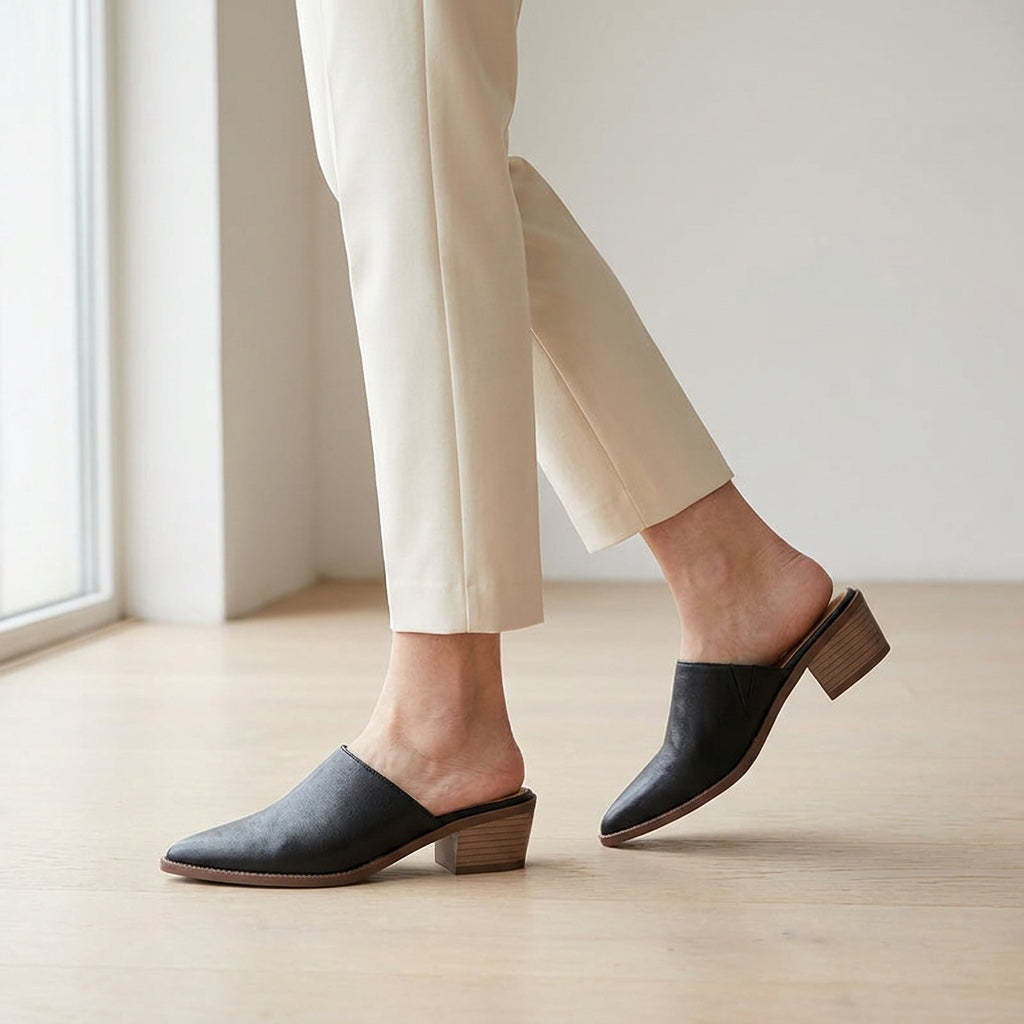 Sabina Leather Mules — Black, worn mid-stride in a gallery interior
