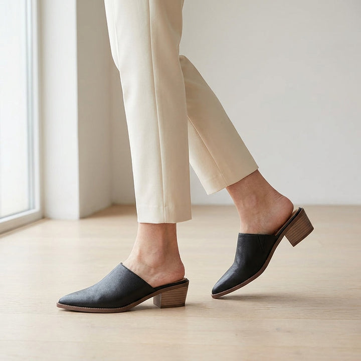 Sabina Leather Mules — Black, worn mid-stride in a gallery interior