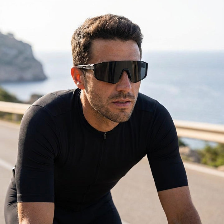 Scilla Shield Sunglasses — Black / Smoke, worn by a man road cycling on a sunny Mallorca coast road