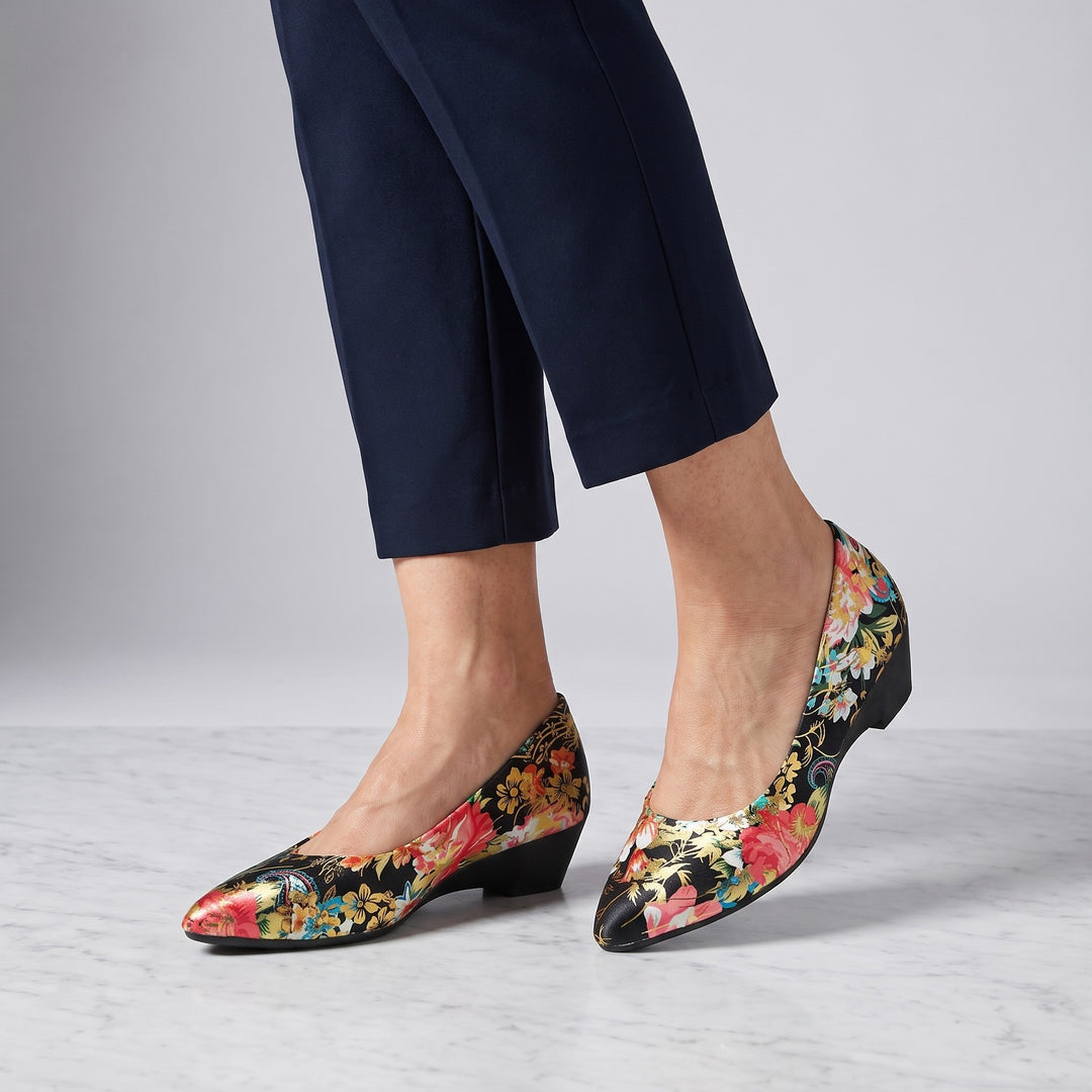 Camogli Floral Pumps — Black Floral, worn by a woman in navy cropped trousers, knee down, on marble