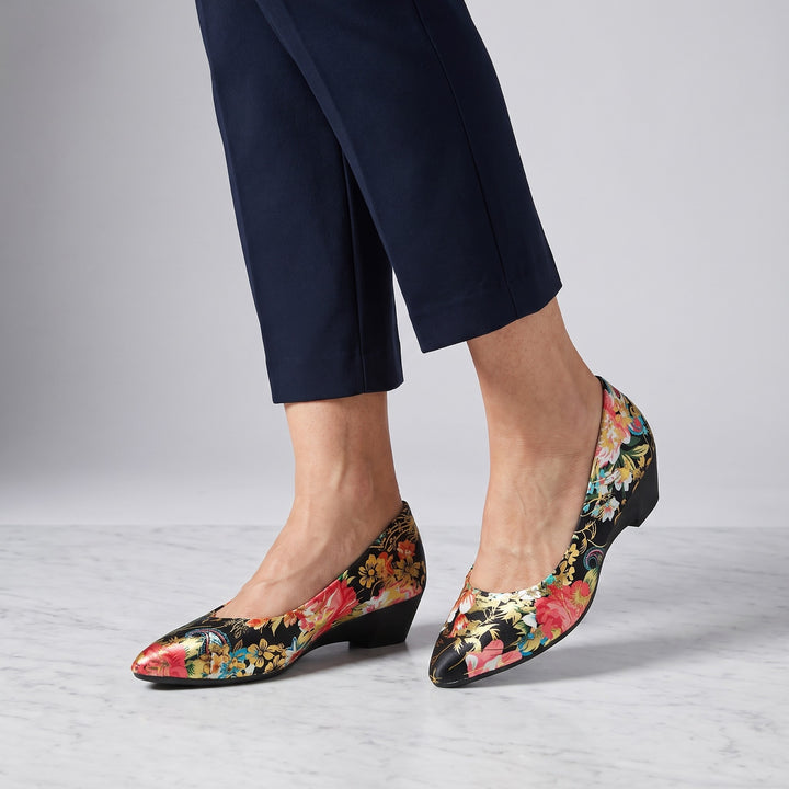 Camogli Floral Pumps — Black Floral, worn by a woman in navy cropped trousers, knee down, on marble