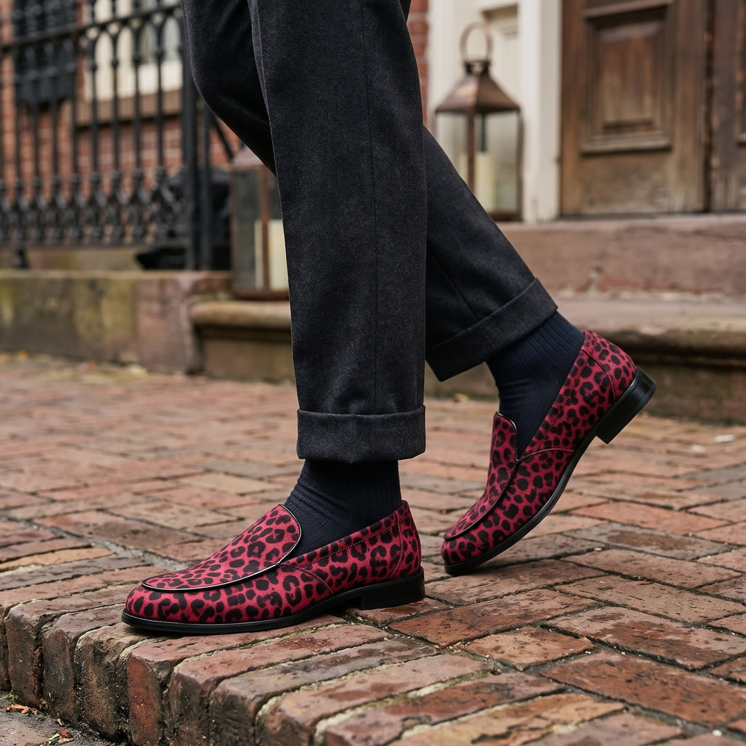 Polignano Leopard Loafers — Red Leopard, worn by a man in charcoal trousers, knee down, on a brick sidewalk outside a historic hotel entrance