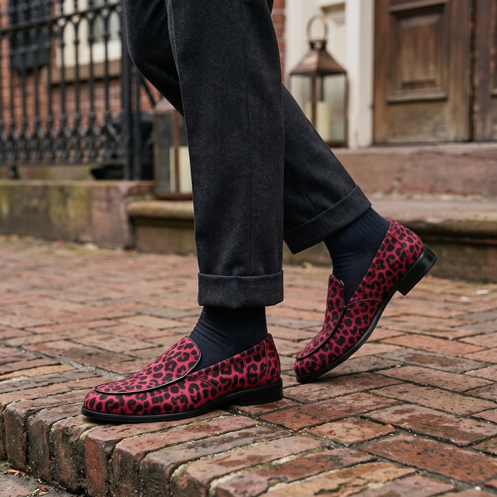 Polignano Leopard Loafers — Red Leopard, worn by a man in charcoal trousers, knee down, on a brick sidewalk outside a historic hotel entrance